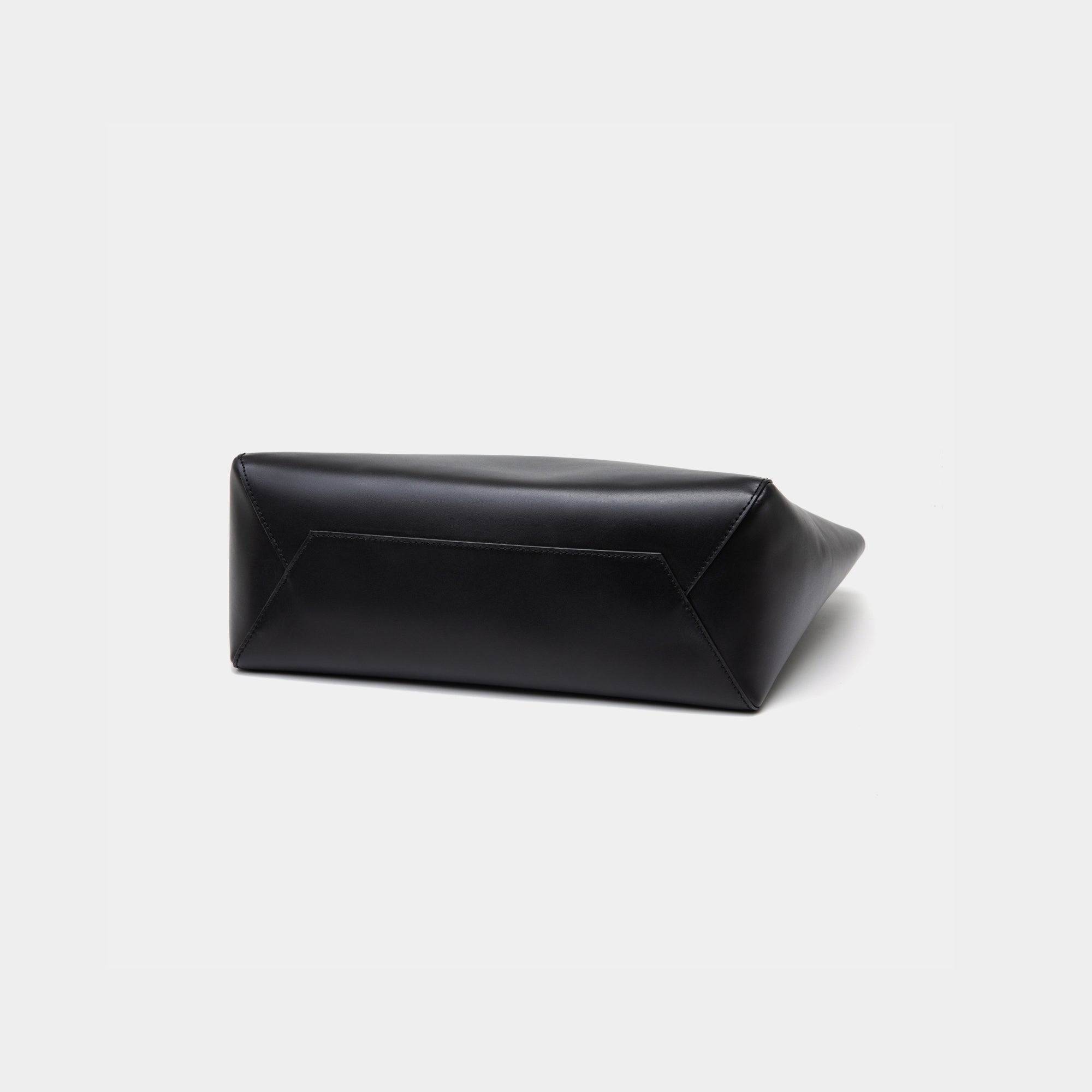 The bottom view of the black MOONSHAFT tote bag displayed against a white background. The bag features a sleek, minimalist design with reinforced stitching along the handles, emphasizing its spacious and structured silhouette.