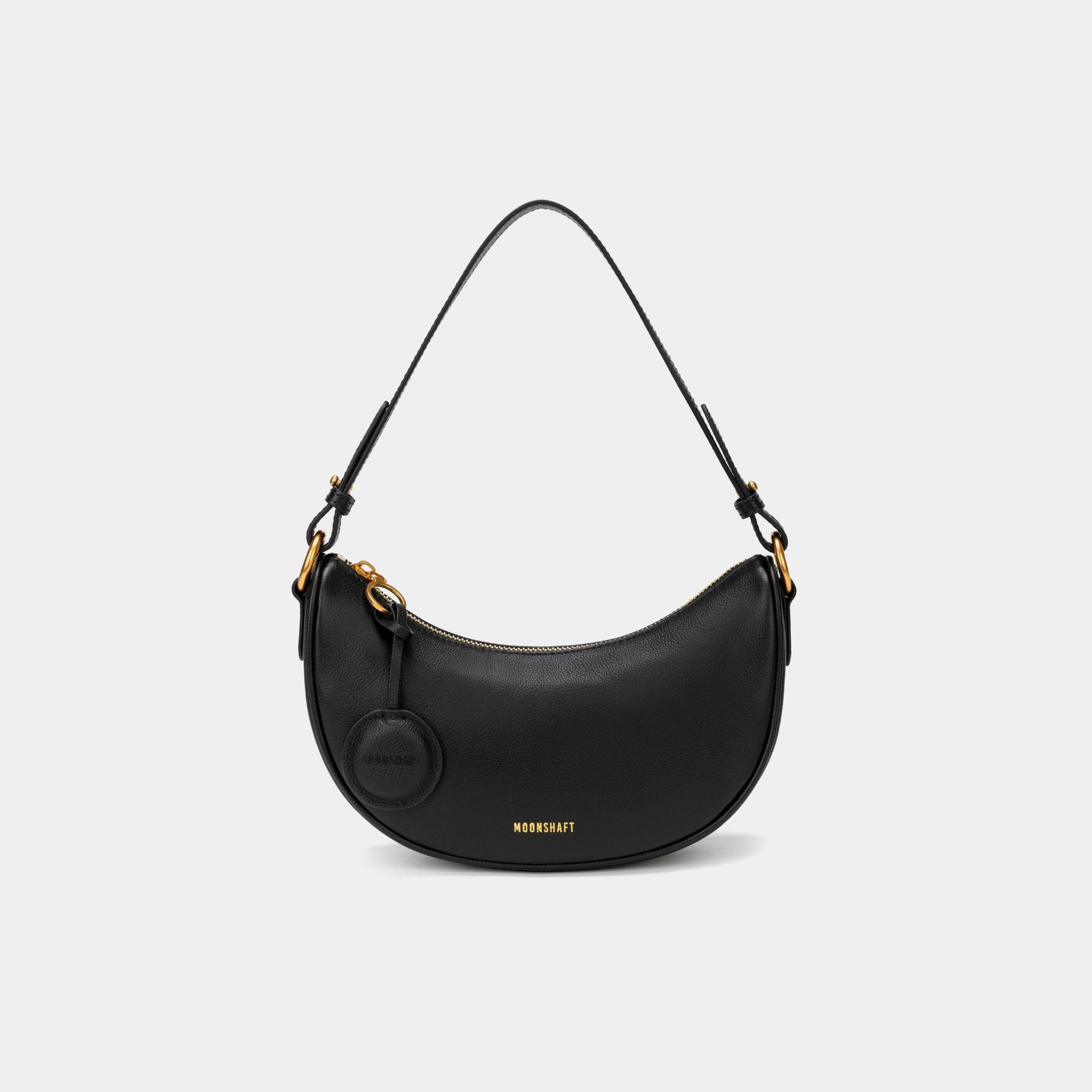 Front view of the Crescent Moon bag in black, showcasing its smooth leather finish, curved silhouette, and gold hardware. The top handle is visible, along with an attached round coin purse accessory on the side. The minimal and elegant design highlights the bag's clean lines and structured shape.