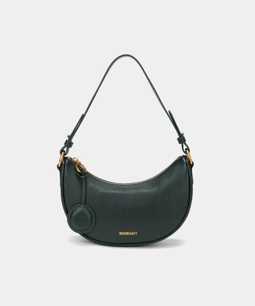 Front view of the Crescent Moon bag in pine grove, showcasing its smooth leather finish, curved silhouette, and gold hardware. The top handle is visible, along with an attached round coin purse accessory on the side. The minimal and elegant design highlights the bag's clean lines and structured shape.