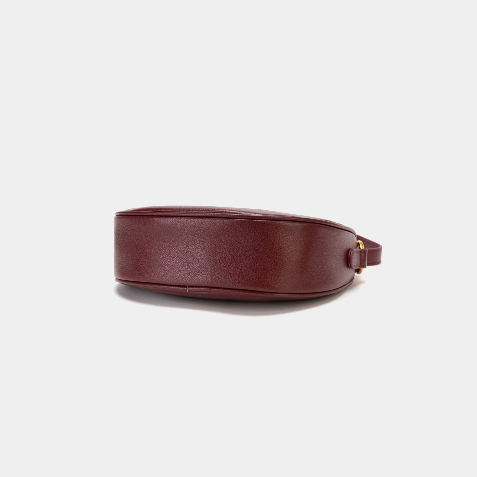 Bottom view of the Crescent Moon bag in wine, showcasing the smooth leather base with a minimalistic and sleek finish. The design emphasizes the clean lines and structure of the bag, with subtle stitching details along the edges. The gold hardware complements the elegant black leather, adding a touch of sophistication.