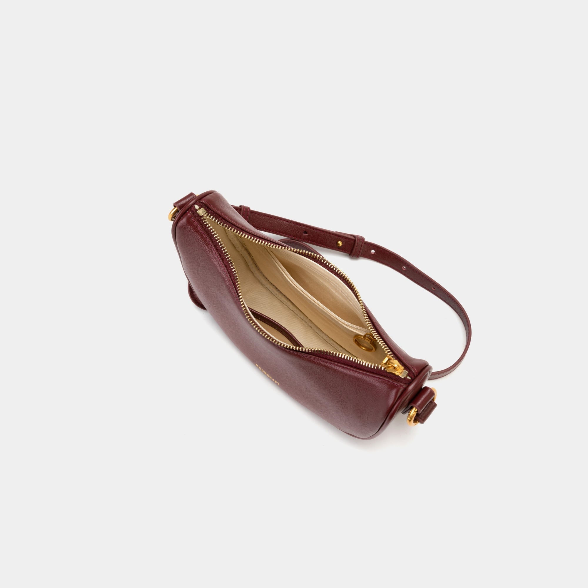 Top view of the Crescent Moon bag in wine, showcasing the smooth leather exterior and gold zipper partially open, revealing the beige interior lining. The inside compartment features a simple yet spacious design with a small slip pocket for organization. The elegant contrast between the black leather and light interior is highlighted.