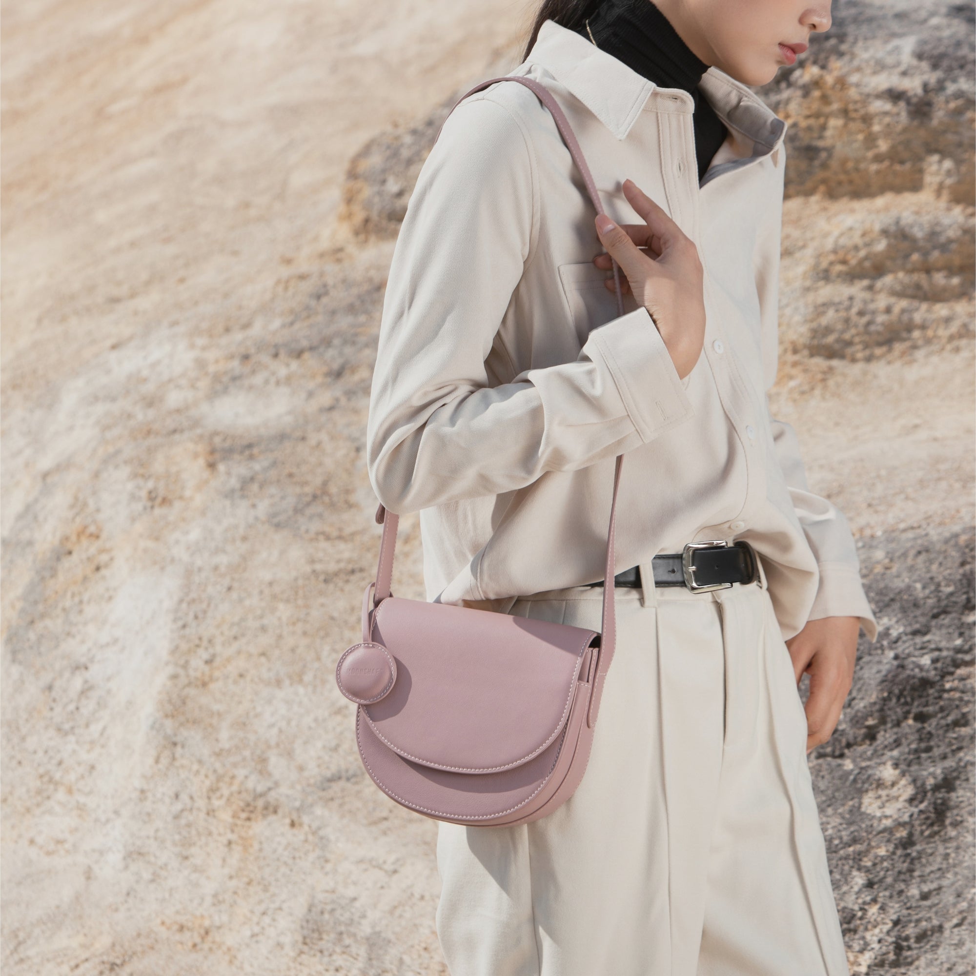 Model wearing a Light Lilac half moon crossbody bag, styled with a casual beige outfit in an outdoor setting, showcasing the bag's structured silhouette and adjustable leather strap.