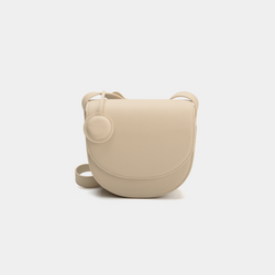 A beige half-moon crossbody bag with a smooth leather finish, featuring a circular leather tag attached to the strap. The structured design highlights the bag's minimalist aesthetic and sleek curves, offering an elegant yet functional style for everyday wear.