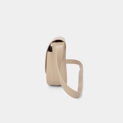 A side view of a beige half-moon crossbody bag showcasing its structured profile. The bag has a sleek, smooth leather finish, and its curved base complements the minimalistic design. The adjustable leather strap and gold-tone hardware are visible from this angle, adding a touch of refinement.
