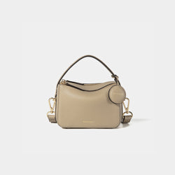 A close-up of the Mini Double Zip Bag in beige color, made from pebbled leather. The bag features a top handle and an adjustable shoulder strap with gold-tone hardware. It has two zippered compartments for storage and a round leather tag attached to the side, embossed with the brand logo 'MOONSHAFT' in gold. The minimalist and structured design enhances its modern and stylish appeal.