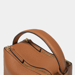 close-up view of the top handle of the Mini Double Zip Bag in toffee color, highlighting the pebbled leather texture. The gold-tone zipper hardware is visible on the two zippered compartments, showcasing the bag's high-quality craftsmanship and attention to detail. The structured handle adds to the bag’s elegant and functional design.