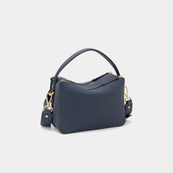 A back view of the upgraded double zip leather bag in marine blue, displayed at a diagonal angle. The pebbled leather texture and structured design are highlighted, with two parallel gold-tone zippers running across the back. The minimalist design and clean lines emphasize the bag’s high-quality craftsmanship.