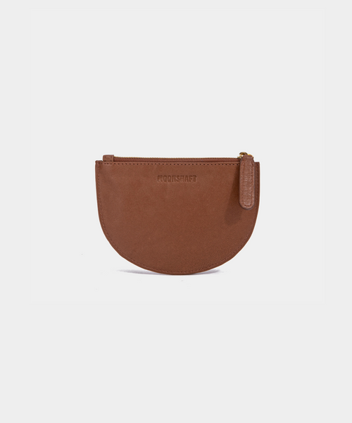 A cognac Half Moon Coin Purse made of goat leather with a zipper on the top and an embossed MOONSHAFT logo on the front.