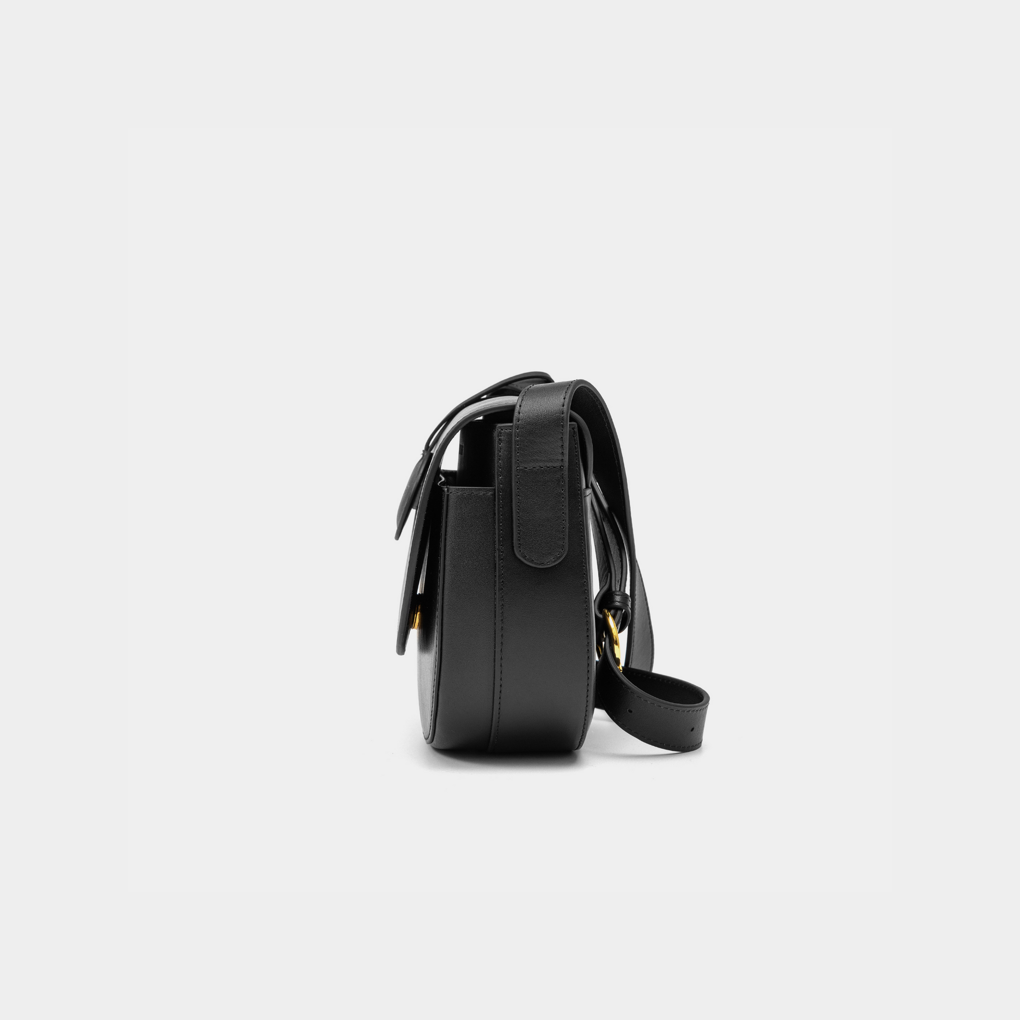 A side view of a black half-moon crossbody bag showcasing its structured profile. The bag has a sleek, smooth leather finish, and its curved base complements the minimalistic design. The adjustable leather strap and gold-tone hardware are visible from this angle, adding a touch of refinement.