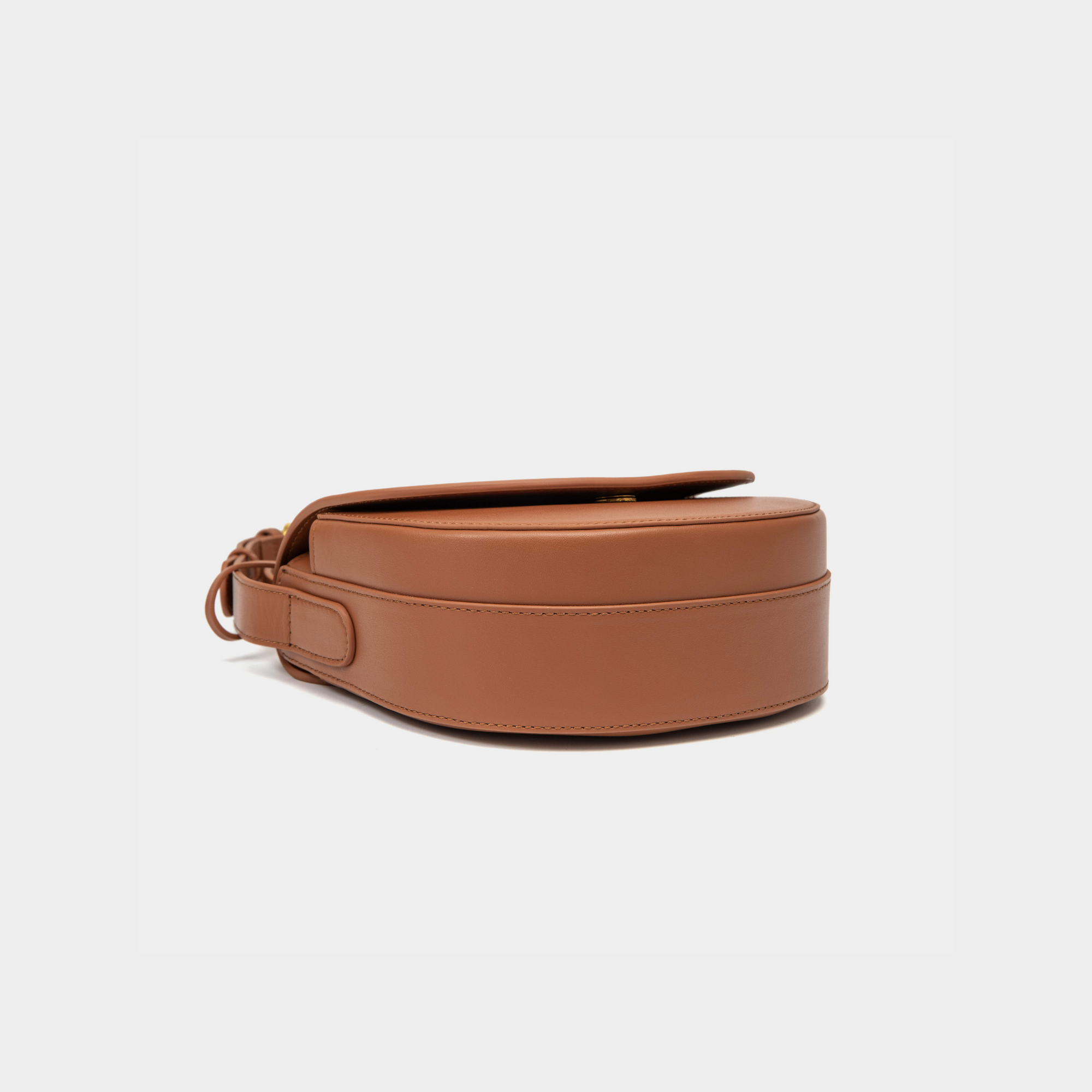 Bottom view of a caramel half moon crossbody bag, highlighting the smooth leather texture and the circular leather tag detail.