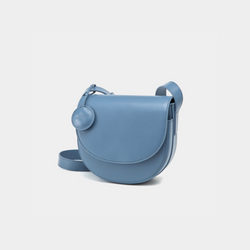 A front-side angle view of a black half-moon crossbody bag made of smooth leather. The bag has a curved base and minimalistic flap closure. A circular leather tag is attached to the strap, adding a subtle design detail. The adjustable strap and sleek design offer a versatile, elegant look.