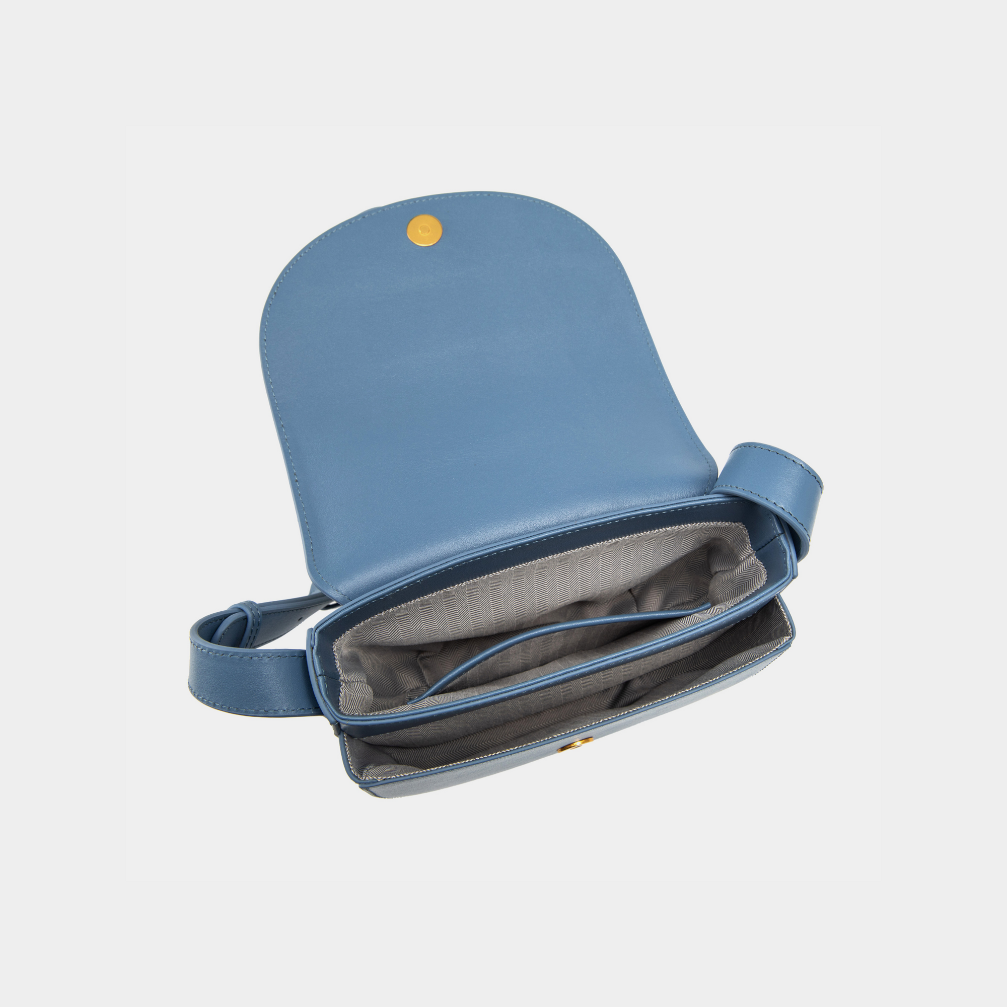 The interior of the stone blue half-moon crossbody bag is revealed, showcasing a smooth flap with a magnetic button closure. The main compartment features an open design, complemented by a neatly stitched inner zip pocket for securing small items. The interior lining has a subtle pattern, adding to the elegance of the bag's craftsmanship.