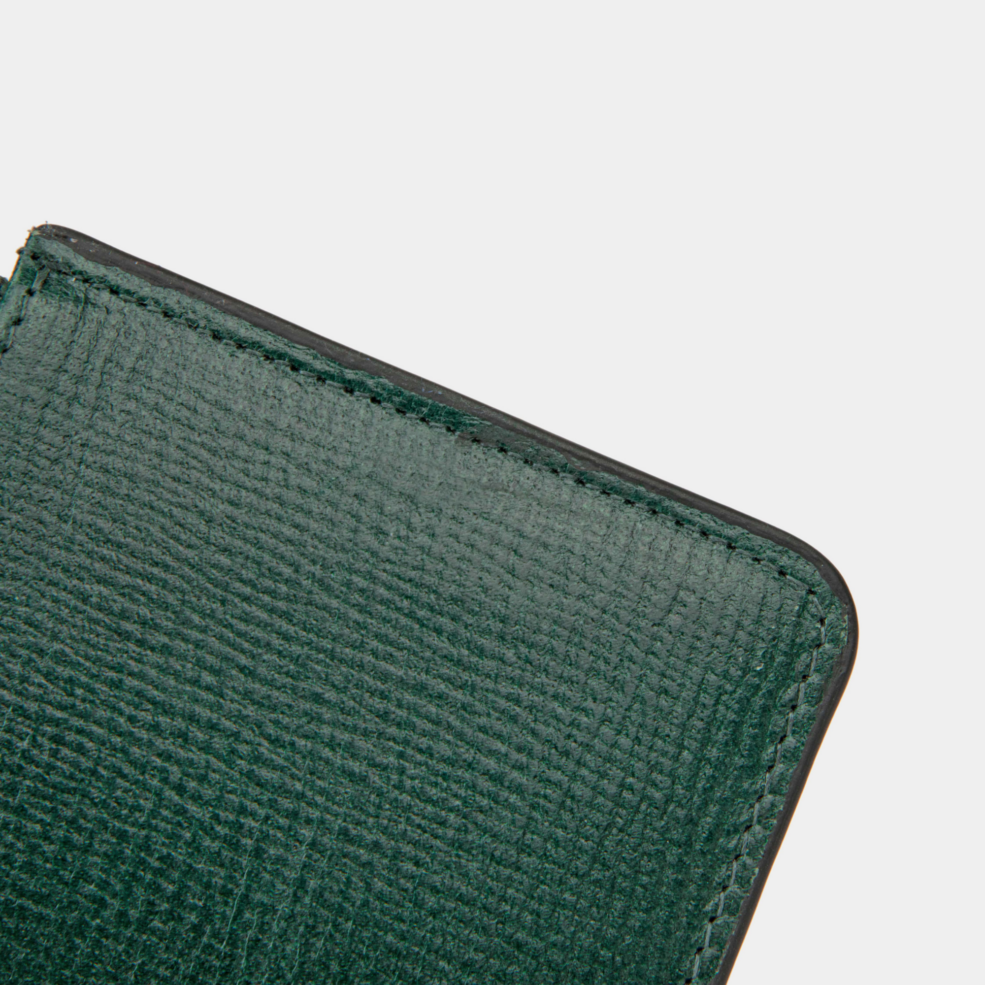 A close-up detail of the top corner of a dark green textured leather cardholder. The stitching is visible along the edge, showcasing the fine craftsmanship and durability of the material. The cardholder features clean, straight stitches, enhancing its structured finish.