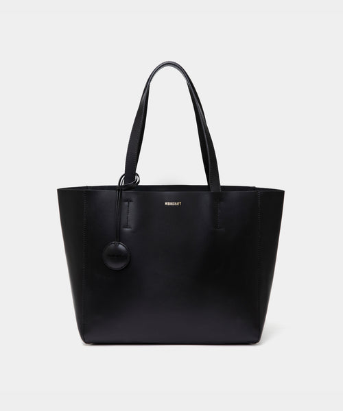 A minimalist black leather tote bag displayed against a plain background. The tote features a smooth leather texture and a clean, structured design with no external embellishments, showcasing its simplicity and elegance. It has two sturdy leather handles and a spacious interior, making it a practical choice for everyday use. The neutral tan color adds to the bag’s versatile appeal, perfect for complementing various outfits and occasions.