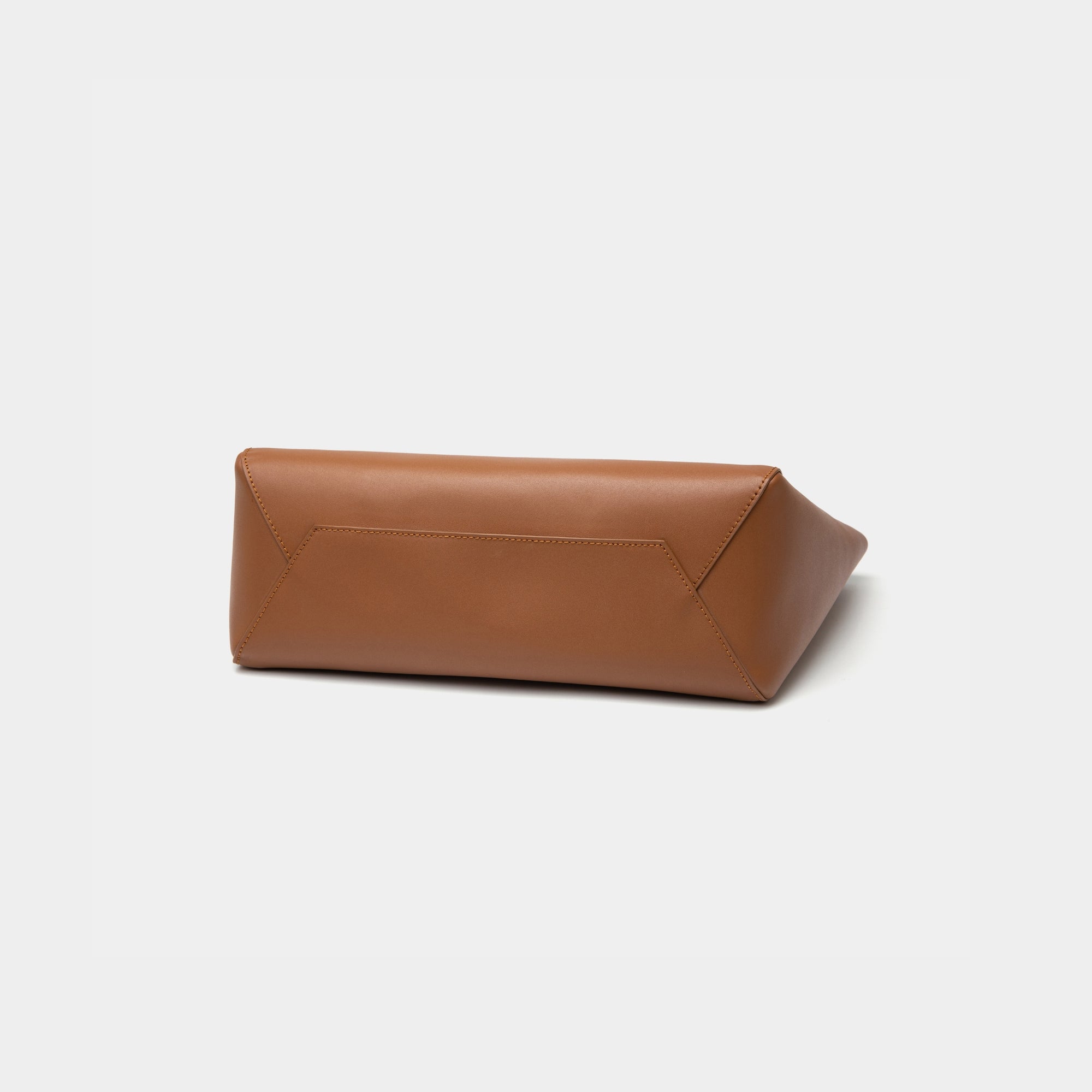 The bottom view of the caramel MOONSHAFT tote bag displayed against a white background. The bag features a sleek, minimalist design with reinforced stitching along the handles, emphasizing its spacious and structured silhouette.