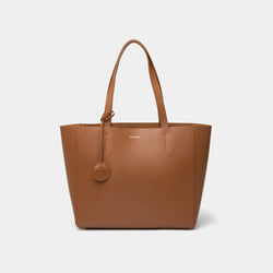 A minimalist caramel leather tote bag displayed against a plain background. The tote features a smooth leather texture and a clean, structured design with no external embellishments, showcasing its simplicity and elegance. It has two sturdy leather handles and a spacious interior, making it a practical choice for everyday use. The neutral tan color adds to the bag’s versatile appeal, perfect for complementing various outfits and occasions.