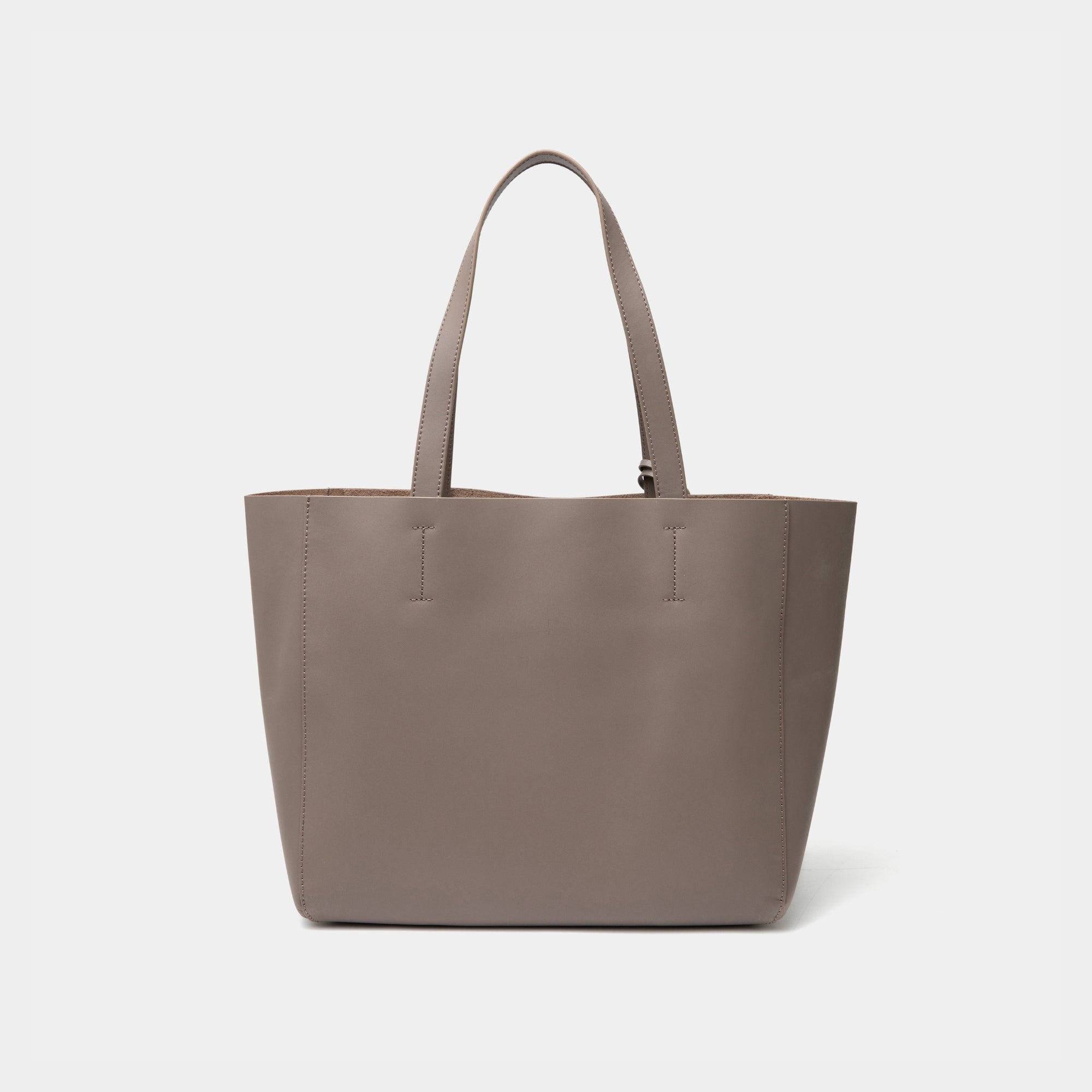 The back view of the taupe MOONSHAFT tote bag displayed against a white background. The bag features a sleek, minimalist design with reinforced stitching along the handles, emphasizing its spacious and structured silhouette.