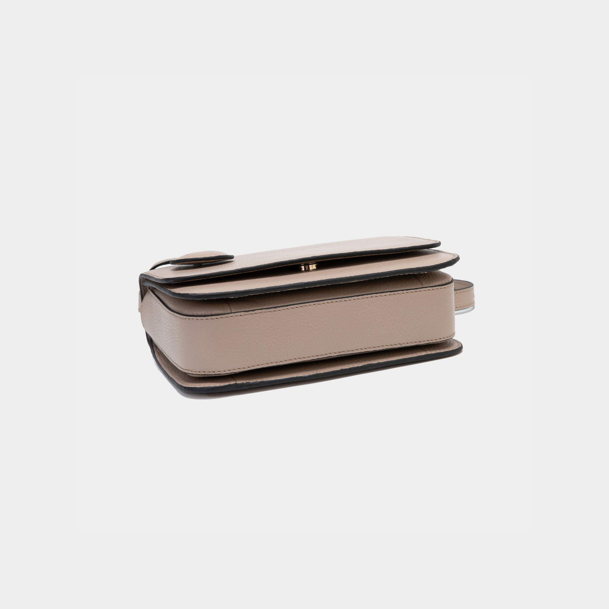 A clay-colored structured boxy bag shown from the underside, highlighting its flat base and sleek, clean lines. The pebbled leather texture and precise stitching emphasize its durable and well-crafted design, suggesting multiple compartments for organized storage.