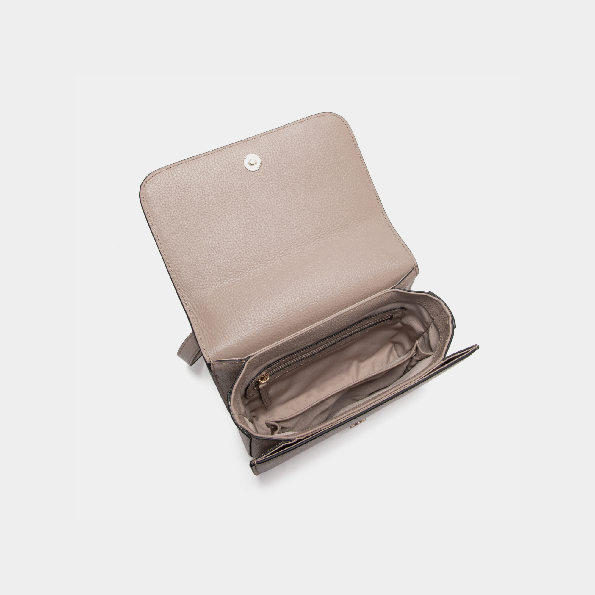 The open view of the clay-colored boxy bag displays its spacious main compartment lined with soft fabric. A zippered pocket is included for secure storage of smaller items. The bag's structured design maintains its shape while offering ample space for everyday essentials. The flap features a metal snap button closure for secure access. The soft pebbled leather finish adds a luxurious and durable touch.