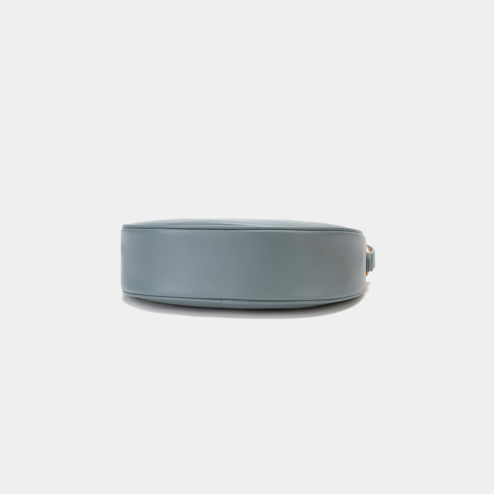  Bottom view of the Crescent Moon bag in ash blue, showcasing the smooth leather base with a minimalistic and sleek finish. The design emphasizes the clean lines and structure of the bag, with subtle stitching details along the edges. The gold hardware complements the elegant black leather, adding a touch of sophistication.