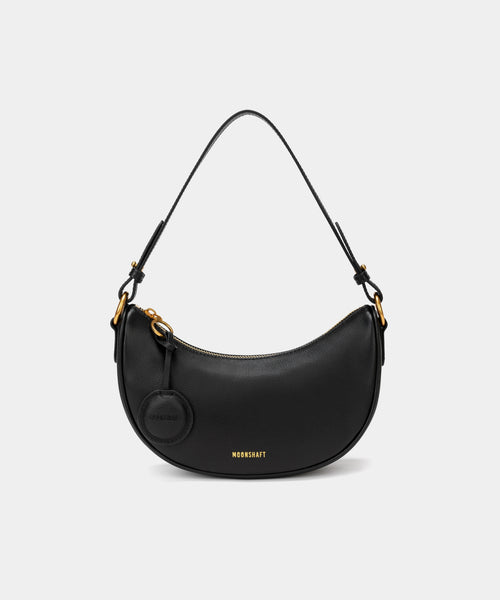 Front view of the Crescent Moon bag in black, showcasing its smooth leather finish, curved silhouette, and gold hardware. The top handle is visible, along with an attached round coin purse accessory on the side. The minimal and elegant design highlights the bag's clean lines and structured shape.