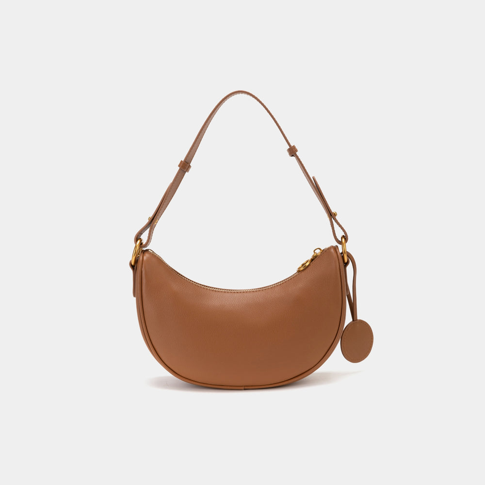 Back view of the Crescent Moon bag in caramel color with a smooth leather finish. The bag features a curved shape, gold hardware, a detachable strap, and a matching leather logo tag. The simple yet elegant design emphasizes the bag’s crescent silhouette, perfect for versatile styling.