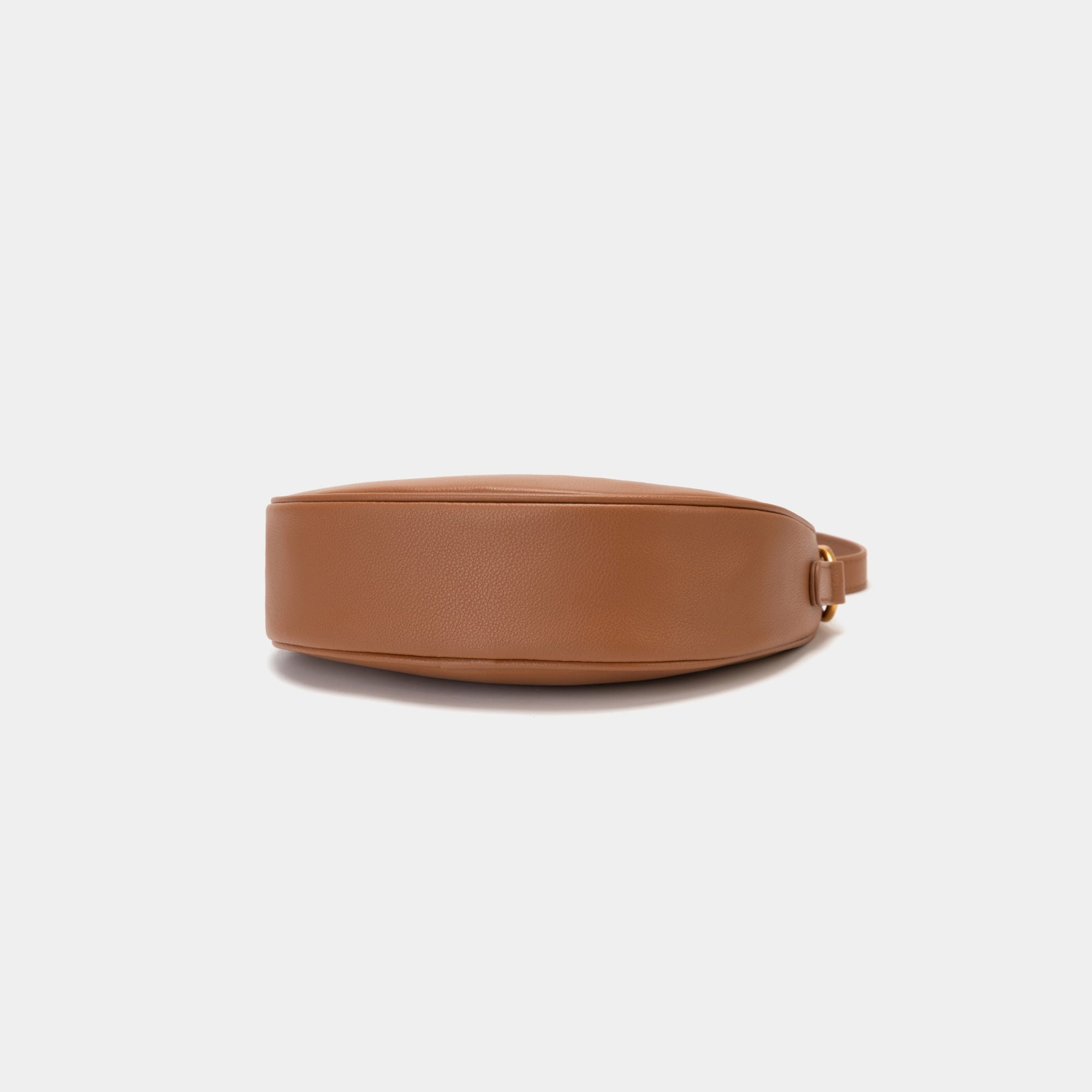  Bottom view of the Crescent Moon bag in caramel, showcasing the smooth leather base with a minimalistic and sleek finish. The design emphasizes the clean lines and structure of the bag, with subtle stitching details along the edges. The gold hardware complements the elegant black leather, adding a touch of sophistication.