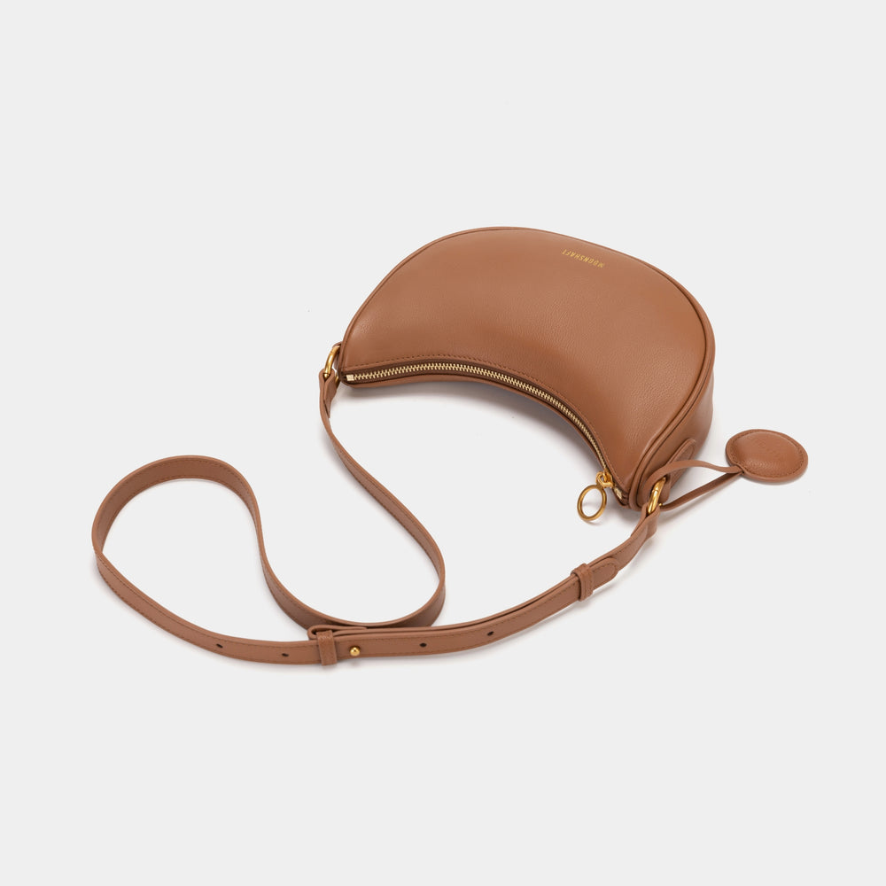 Top-down view of the Crescent Moon bag in caramel, laying flat with its long strap extended. The image highlights the gold zipper detail and the structured design, perfect for keeping essentials secure.