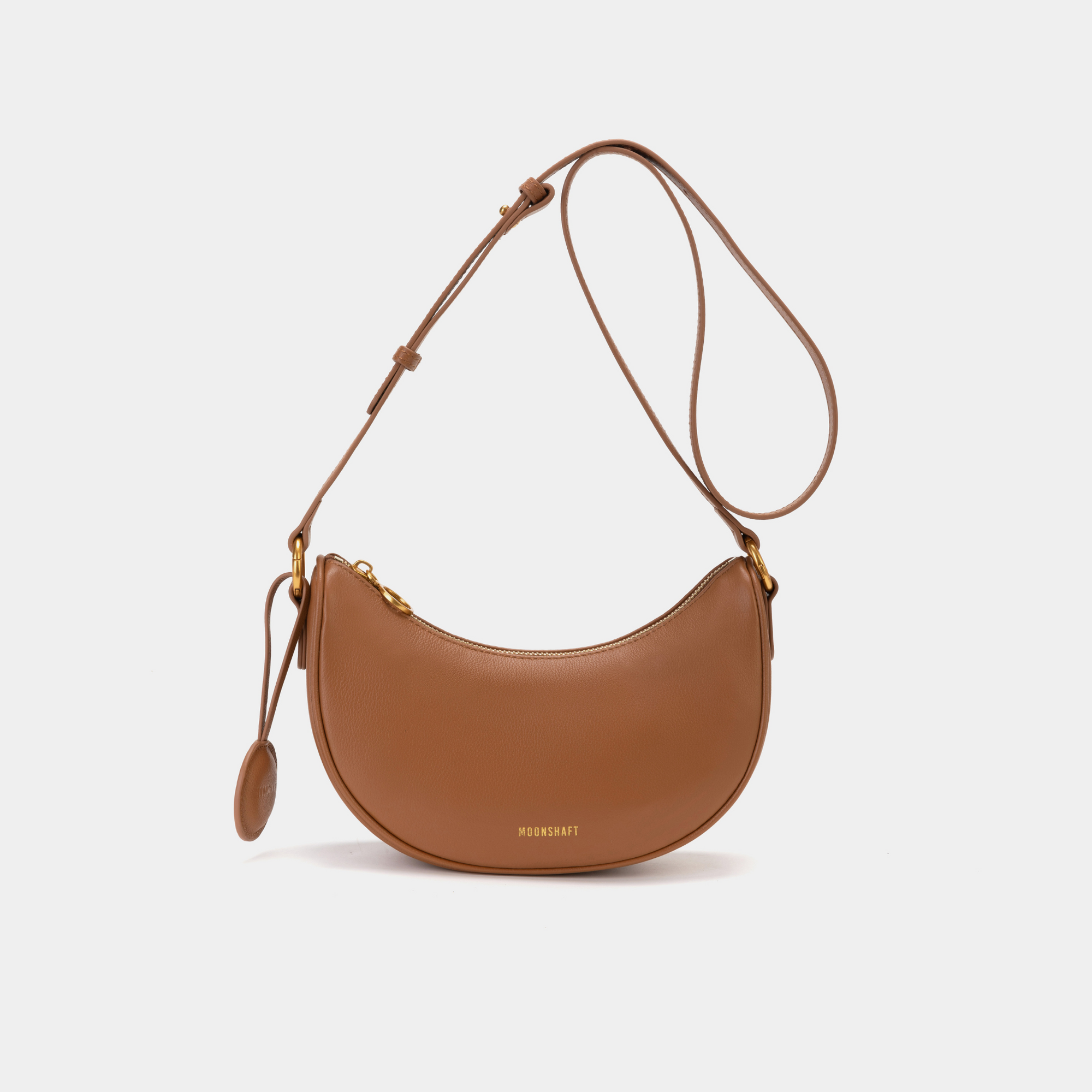 Front view of the Crescent Moon bag in caramel, featuring smooth leather with a minimalist design. The bag is shown with its adjustable crossbody strap and gold-tone hardware, highlighting the curved silhouette and simple elegance of the design.