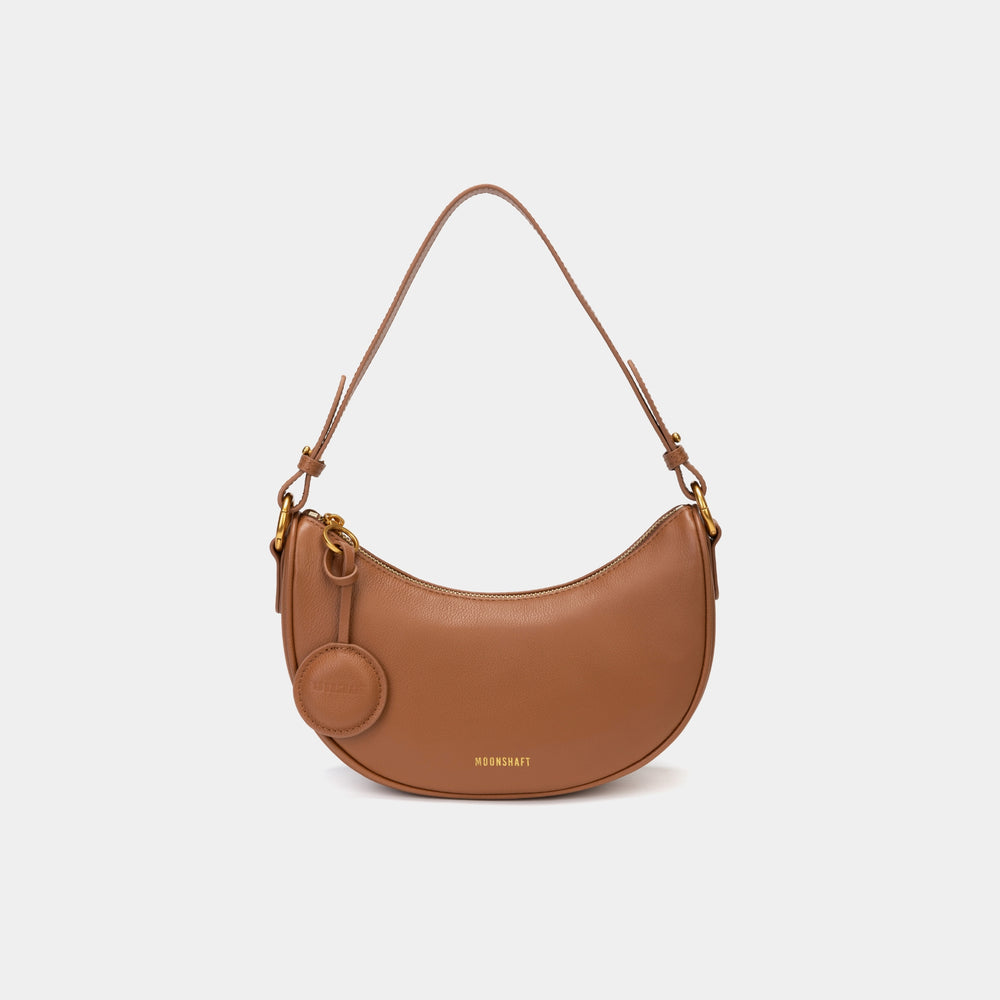 Front view of the Crescent Moon bag in caramel, showcasing its smooth leather finish, curved silhouette, and gold hardware. The top handle is visible, along with an attached round coin purse accessory on the side. The minimal and elegant design highlights the bag's clean lines and structured shape.