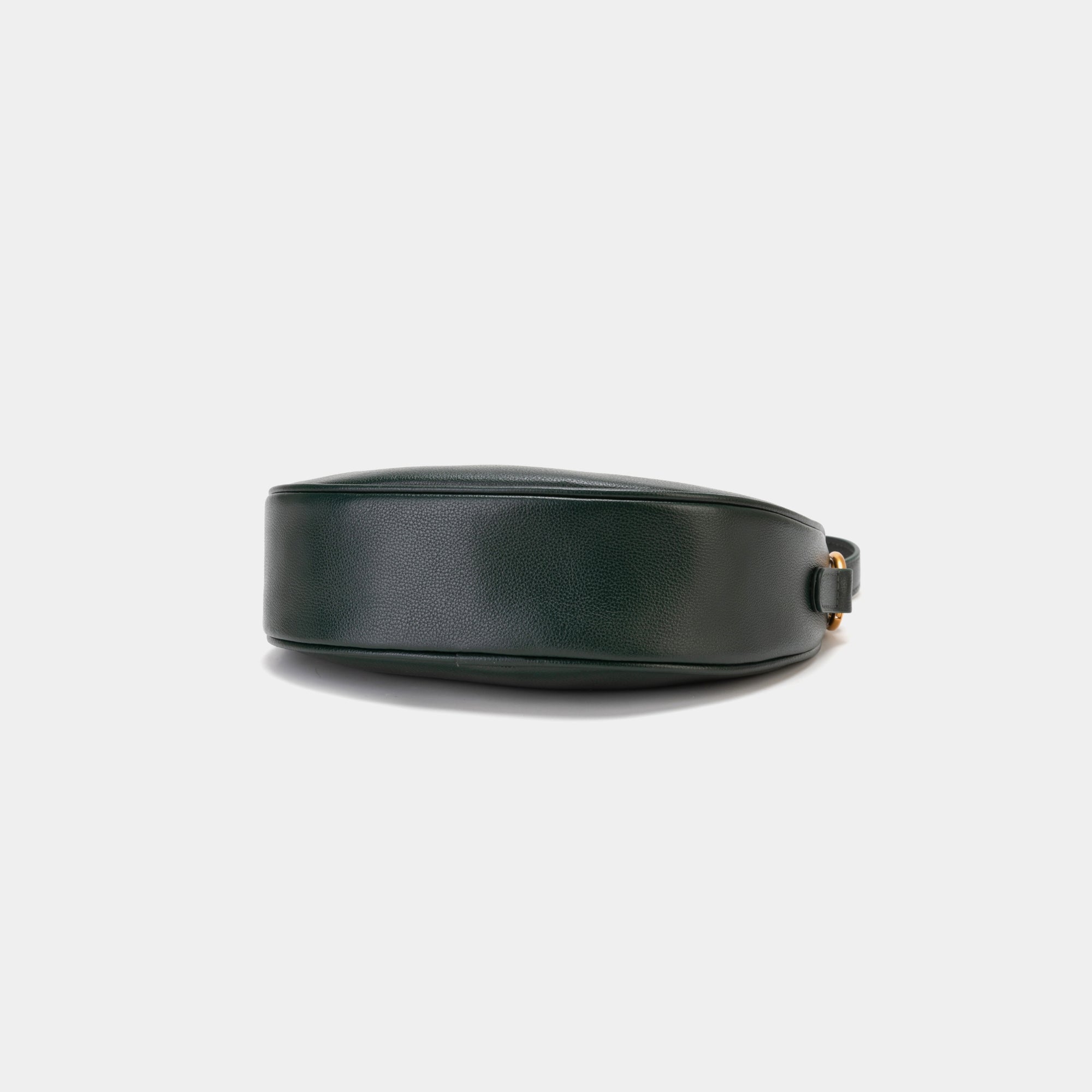  Bottom view of the Crescent Moon bag in pine grove, showcasing the smooth leather base with a minimalistic and sleek finish. The design emphasizes the clean lines and structure of the bag, with subtle stitching details along the edges. The gold hardware complements the elegant black leather, adding a touch of sophistication.