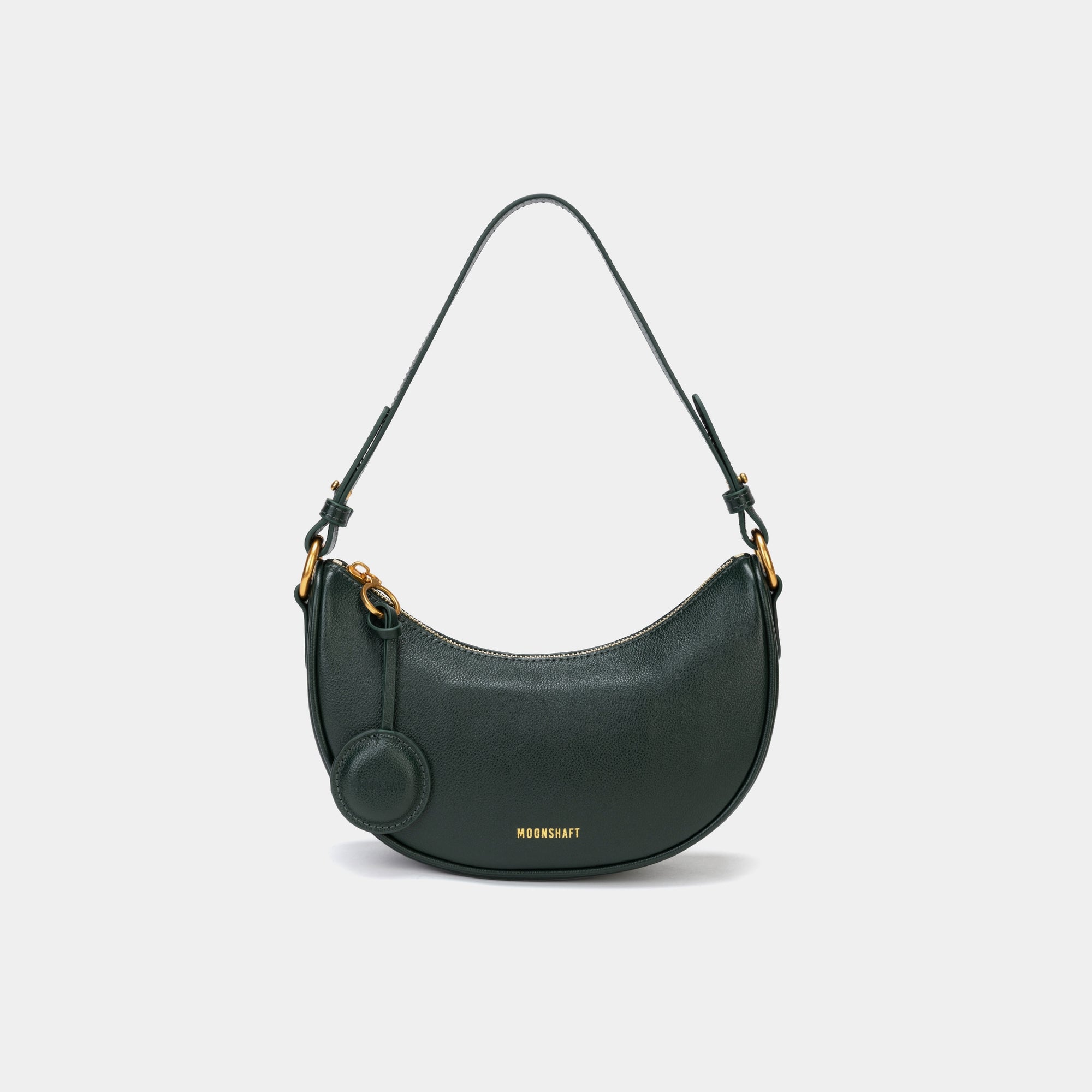 Front view of the Crescent Moon bag in pine grove, showcasing its smooth leather finish, curved silhouette, and gold hardware. The top handle is visible, along with an attached round coin purse accessory on the side. The minimal and elegant design highlights the bag's clean lines and structured shape.