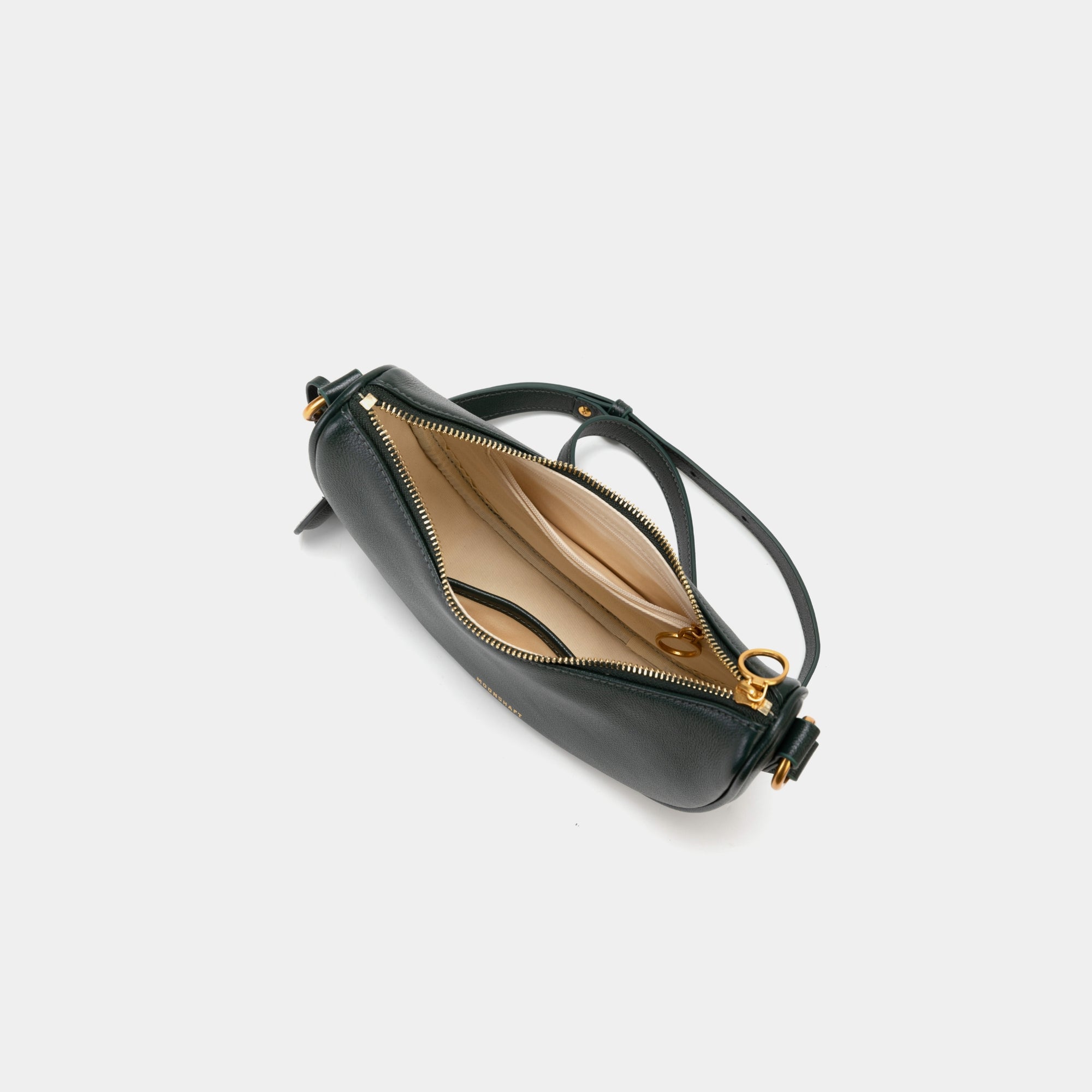 Top view of the Crescent Moon bag in pine grove, showcasing the smooth leather exterior and gold zipper partially open, revealing the beige interior lining. The inside compartment features a simple yet spacious design with a small slip pocket for organization. The elegant contrast between the black leather and light interior is highlighted.