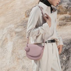 Model wearing a Light Lilac half moon crossbody bag, styled with a casual beige outfit in an outdoor setting, showcasing the bag's structured silhouette and adjustable leather strap.