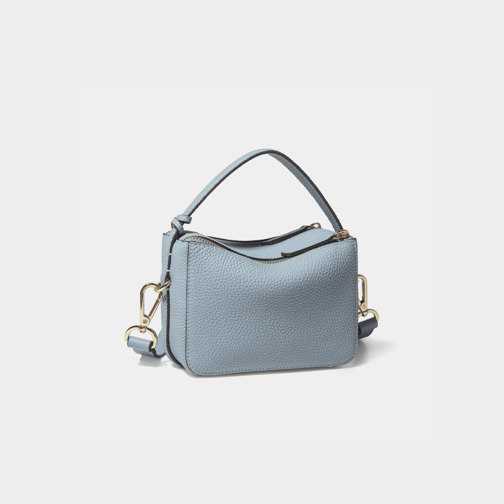 A diagonal back view of the Mini Double Zip Bag in aqua marine color, crafted from pebbled leather. The bag features a smooth and structured design with a top handle and detachable gold-tone hardware. The clean back panel showcases the minimalist style, while the adjustable shoulder strap and two zippered compartments add both functionality and elegance to the overall look.