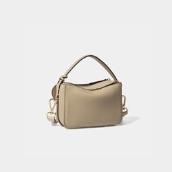 A diagonal back view of the Mini Double Zip Bag in beige color, crafted from pebbled leather. The bag features a smooth and structured design with a top handle and detachable gold-tone hardware. The clean back panel showcases the minimalist style, while the adjustable shoulder strap and two zippered compartments add both functionality and elegance to the overall look.