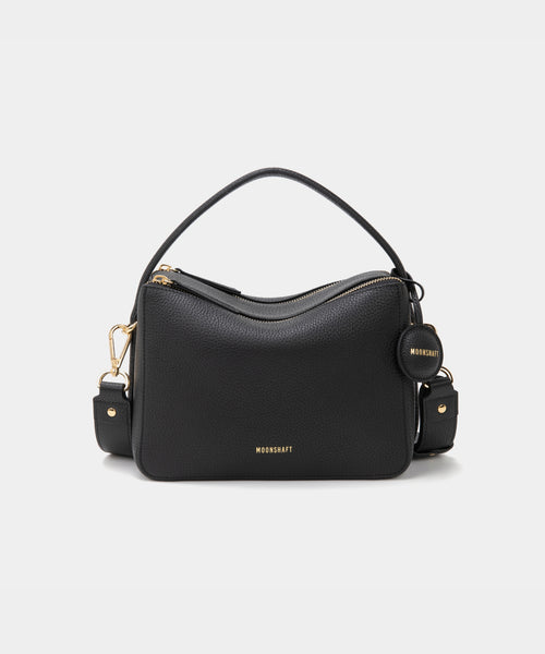 A black-colored upgraded double zip leather bag displayed from a front angle against a plain background. The bag showcases a minimalist design with pebbled leather and two prominent zippered compartments. The structured form and gold-tone zippers add both functionality and a sleek, modern touch. The neutral sandstone color enhances the bag's versatile appeal, making it suitable for a variety of outfits and occasions.