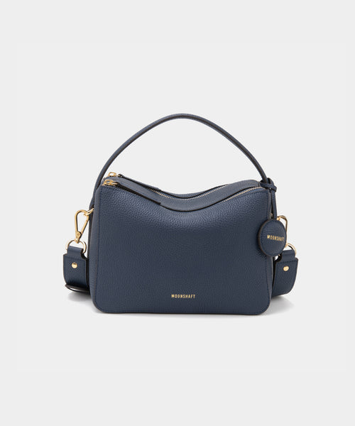 A marineblue-colored upgraded double zip leather bag displayed from a front angle against a plain background. The bag showcases a minimalist design with pebbled leather and two prominent zippered compartments. The structured form and gold-tone zippers add both functionality and a sleek, modern touch. The neutral marine blue color enhances the bag's versatile appeal, making it suitable for a variety of outfits and occasions.