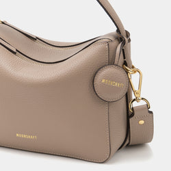 ag with the MOONSHAFT logo embossed in gold. The smooth, pebbled leather texture is highlighted, along with the structured design and elegant gold-tone zippers. The detachable strap is secured with a gold-tone clasp, and a circular leather charm with 'MOONSHAFT' embossed in gold hangs from the side, adding a stylish detail. The soft sandstone color enhances the bag's minimalist and refined appearance.