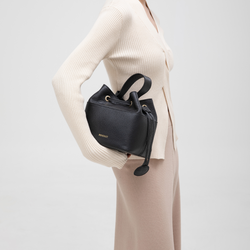 Model carrying a black pebbled leather bucket bag with a drawstring closure, showcasing a stylish yet practical accessory for everyday use.