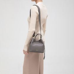 Model carrying a gray pebbled leather bucket bag with a long crossbody strap and drawstring closure, highlighting a versatile and chic everyday accessory.