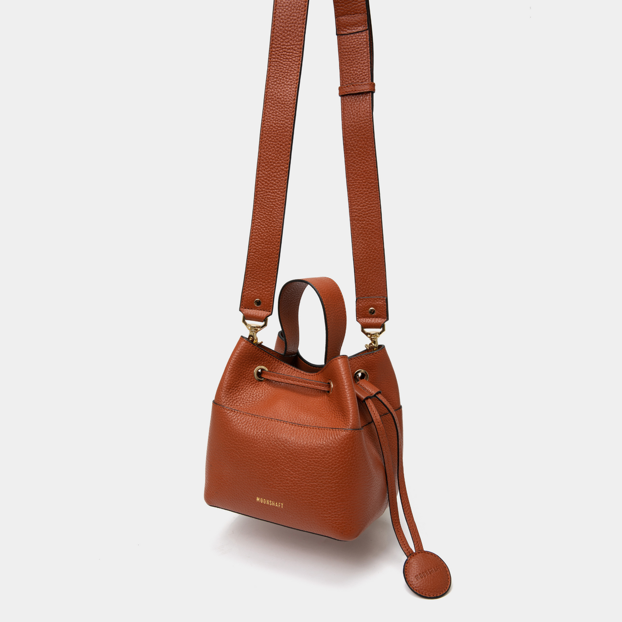 Tan pebbled leather bucket bag with an adjustable wide shoulder strap for comfortable wear. The drawstring closure and coin pouch detail enhance both its practicality and stylish design.