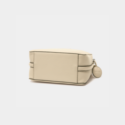 A bottom view of the MOONSHAFT double zip pebbled leather bag in sand, highlighting the structured rectangular base with clean stitching along the edges. The smooth pebbled leather texture is prominent, and the side profile reveals the compact, sleek design of the bag. A glimpse of the attached round leather charm is visible to the side.