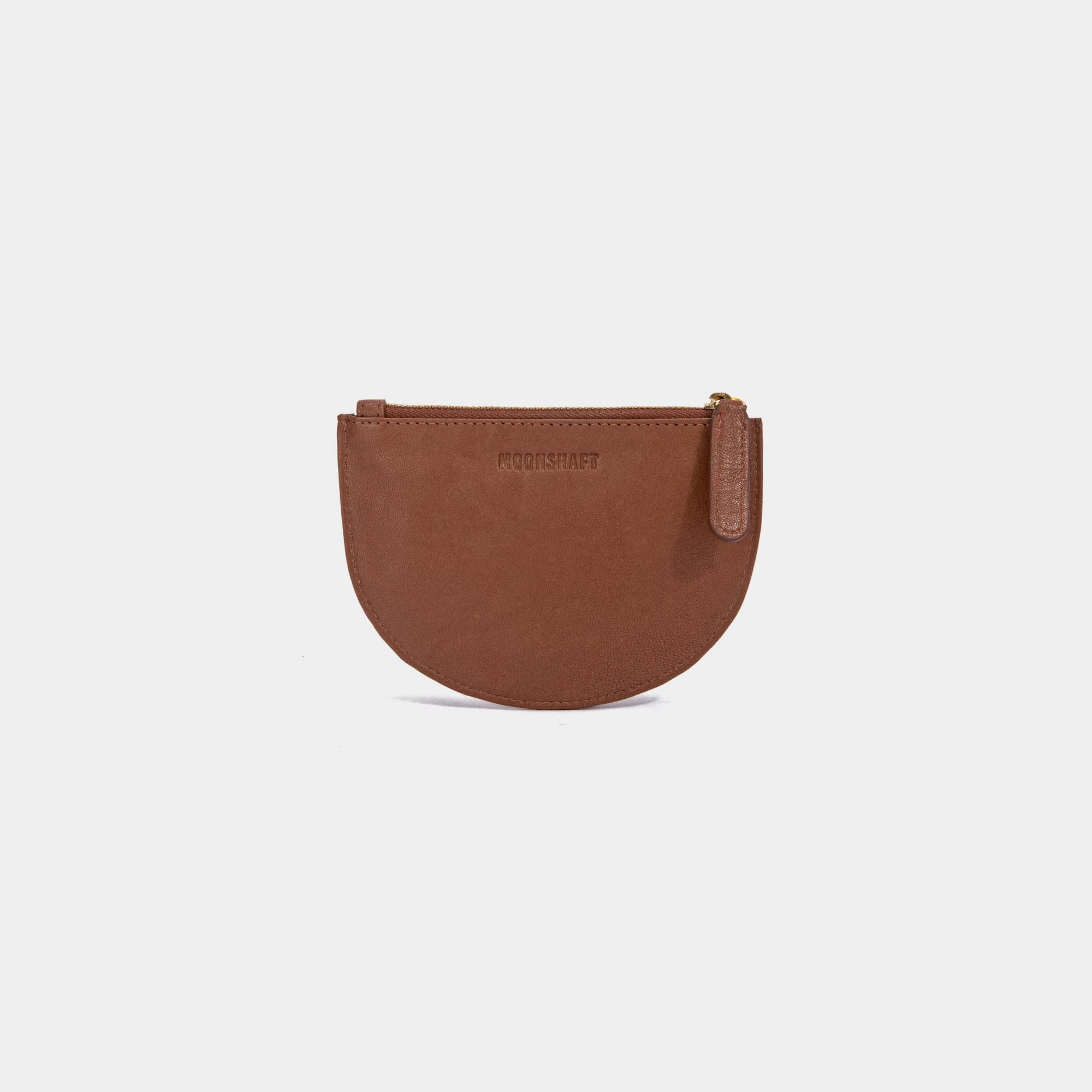 A cognac Half Moon Coin Purse made of goat leather with a zipper on the top and an embossed MOONSHAFT logo on the front.