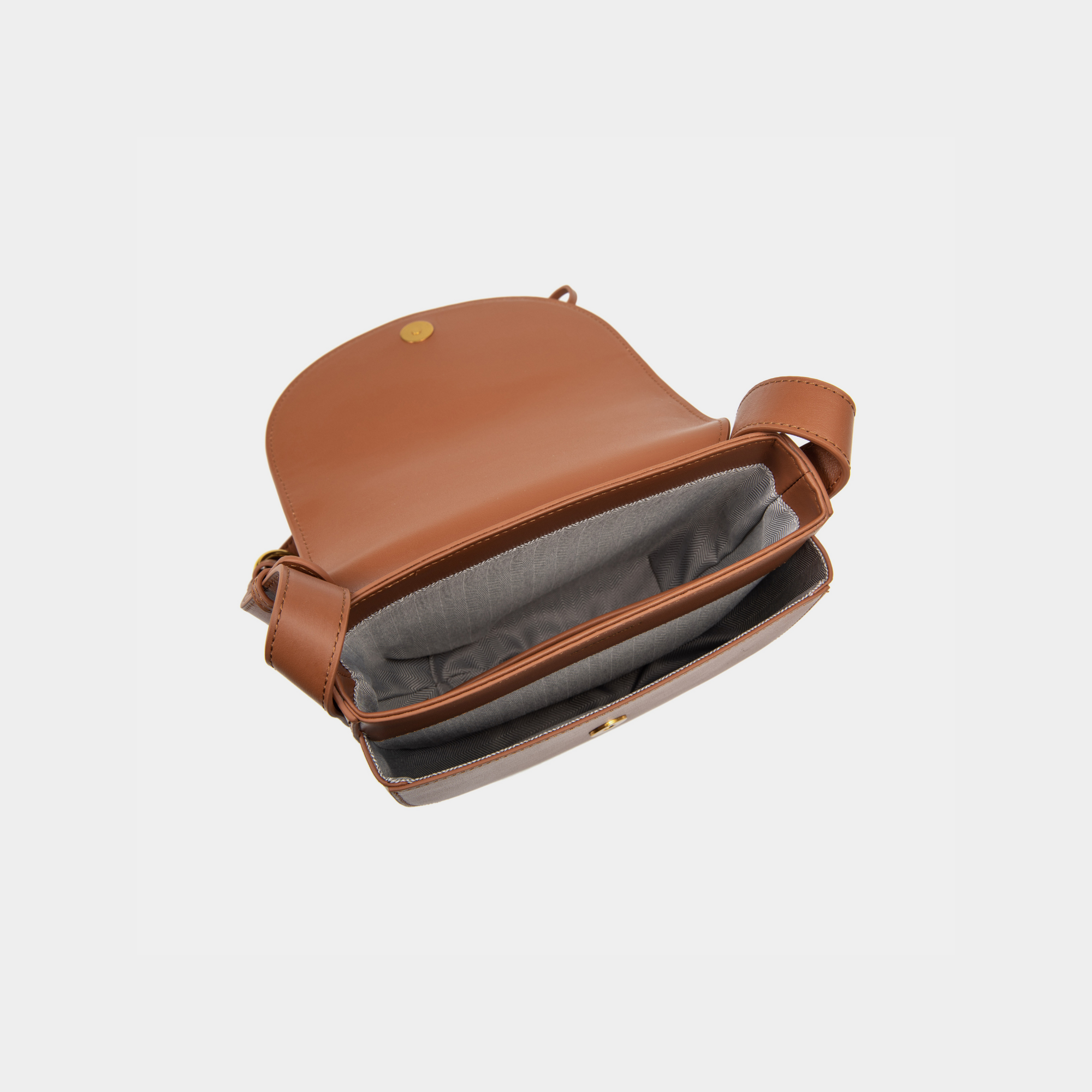 The interior of the caramel half-moon crossbody bag is revealed, showcasing a smooth flap with a magnetic button closure. The main compartment features an open design, complemented by a neatly stitched inner zip pocket for securing small items. The interior lining has a subtle pattern, adding to the elegance of the bag's craftsmanship.