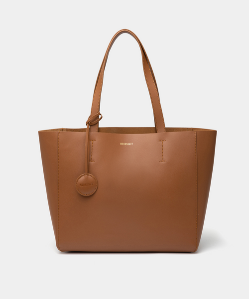 A caramel leather tote bag displayed from the front, highlighting its minimalist and structured design. The bag features a smooth leather texture with no external pockets or embellishments, emphasizing its sleek and elegant appearance. Two sturdy leather handles are visible, and the black color enhances its versatility, making it a stylish accessory for various outfits and occasions. The clean lines and spacious design offer practicality, making this tote suitable for everyday use.