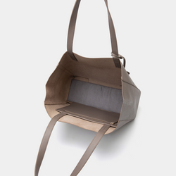 A taupe leather tote bag displayed from a top-down angle with the bag open, revealing its spacious interior. The smooth leather exterior maintains the minimalist design, while the inside shows a roomy, unlined compartment, ideal for carrying everyday essentials. The long leather handles are visible, adding to the bag’s practicality and functionality. The neutral taupe color enhances the bag’s versatility, making it a stylish and practical choice for various occasions.
